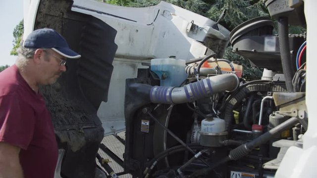 Truck driver with hood of semi truck open inspecting engine