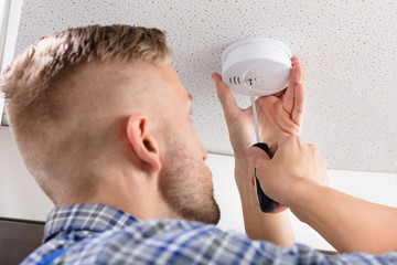 Person's Hand Using Screwdriver To Install Smoke Detector