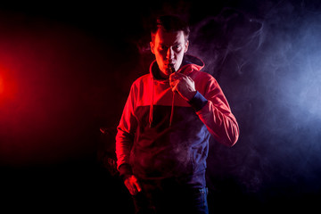 Fototapeta na wymiar The man smoke an electronic cigarette, vape on a background of red and white smoke