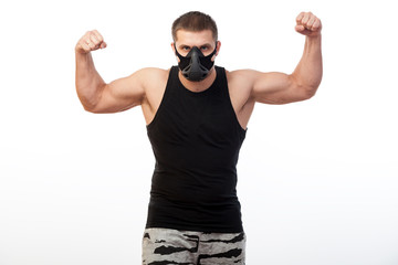 A young athletic man  boxer in a sports T-shirt, training black mask showing his biceps and standing on white isolated background