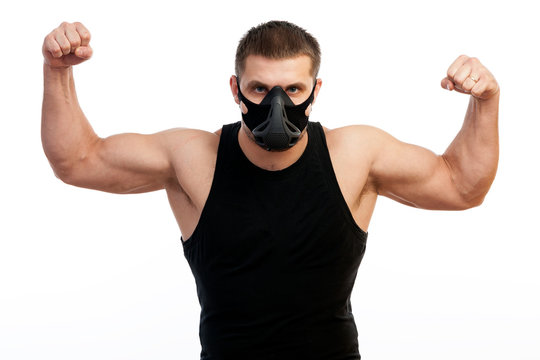 A young athletic man  boxer in a sports T-shirt, training black mask showing his biceps and standing on white isolated background