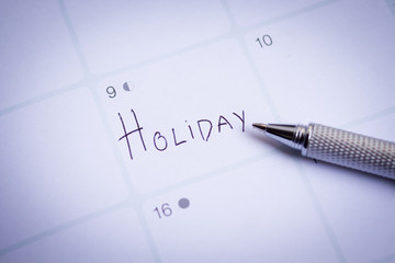 Text "HOLIDAY" written with a pen on a white paper. Image use for holiday background.
