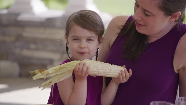 Young girl eating corn at backyard barbeque