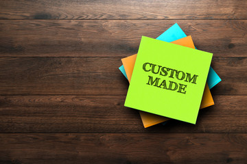 Custom Made, the phrase is written on multi-colored stickers, on a brown wooden background. Business concept, strategy, plan, planning.