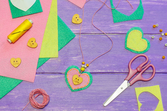 Simple felt heart pendant necklace. Valentines day pendant necklace made of felt, beads and wooden button with text love. Kids art workplace. Gift for mum. Fun creative art activity for preschoolers