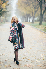 Portrait in full growth, attractive young blonde woman in black dress walking in autumn park