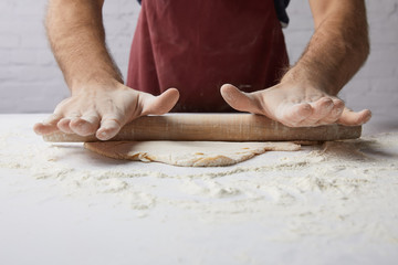 cropped image of chef rolling dough with rolling pin