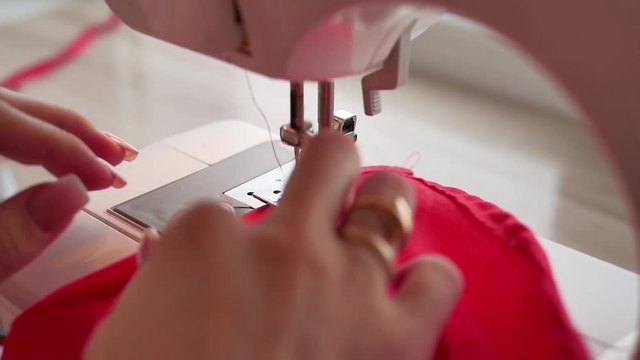 Woman sews on the modern sewing machine. Sewing machine sews close up the action in slow motion.