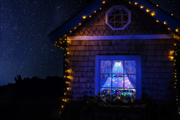 A fairy-tale house with garlands and a Christmas tree in a window under a starry sky. Magic winter night photo.
