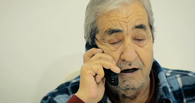 Grandfather of eighty-two years talking to his friend on the phone sitting on a chair in the room.