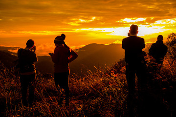 Photo silhouette and travel.They are stading on mountains and see the sunset / sunup. A man take photo and woman play mobile phone. they are fun .