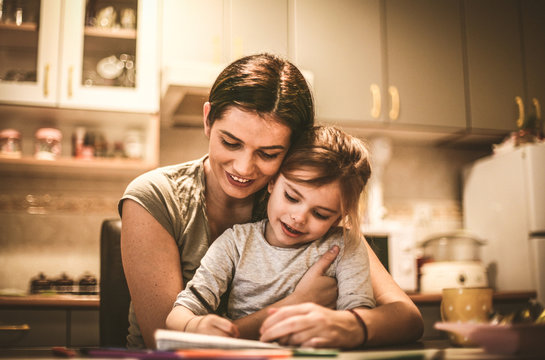 Little girl sit in mothers lap and drawing.