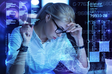 Facing problems. Clever reliable enthusiastic woman sitting with her head leaning on her hand and looking thoughtful while sitting in front of a transparent screen