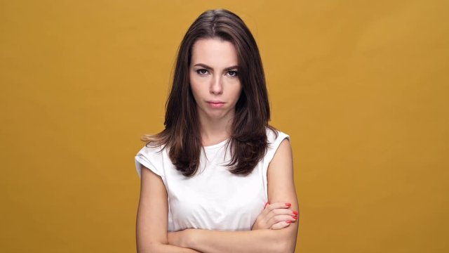 Young sad woman standing isolated over yellow background while looking camera with arms crossed.
