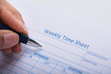 Person Filling Weekly Time Sheet With Pen