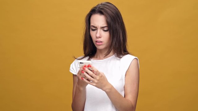 Young sad woman standing isolated over yellow background while chatting by mobile phone
