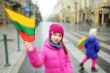 Two adorable little sisters celebrating Lithuanian Independence Day holding tricolor Lithuanian flags