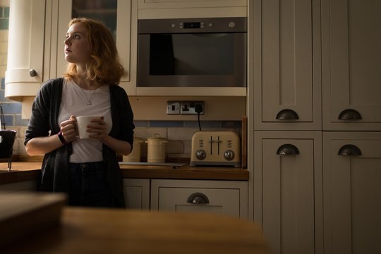 Thoughtful woman having coffee while standing in kitchen