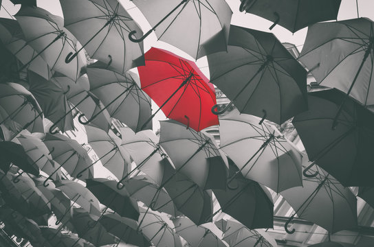 Red different umbrella in mass of black umbrellas