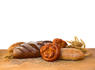 Assorted different fresh baked bread, dark and white whole grain loaves, wheat ears and wheat grain on wooden table on a white background