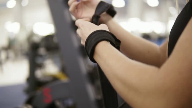 Young attractive female bodybuilder ties fitness straps around barbellpreparing to train. Fitness and workout. Healthcare.