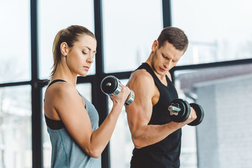 side view of couple in sportswear training with dumbbells in gym