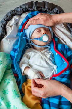 Mothers hands holding a sick infant boy patient with a pacifier and bandage on his hand, seen from above.
