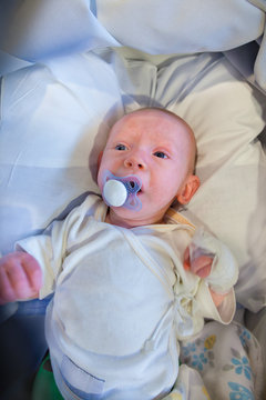 Sick infant boy with a pacifier and bandage on his hand lies on the back on several pillows