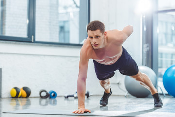 Naklejka na ściany i meble handsome shirtless young sportsman doing push ups on yoga mat