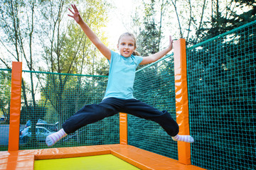 Happy caucasian girl jumping high on a trampoline on a sunny day outdoors.