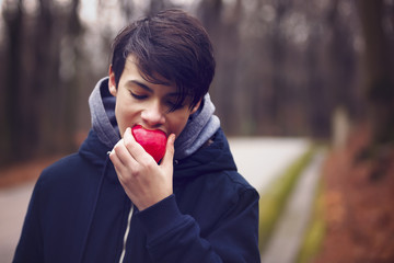 young man eating a red apple in the park