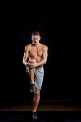 Fototapeta premium muscular young sportsman holding knee in hands and looking at camera on black