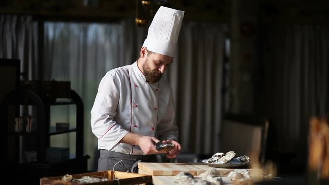 Chef in a luxury restaurant opens oysters and puts them on a plate with ice