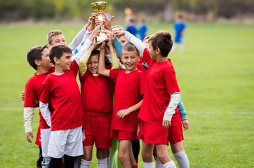 Afwasbaar Fotobehang Voetbal Kinder voetbal voetbal - kinderen spelers vieren met een trofee na wedstrijd op voetbalveld
