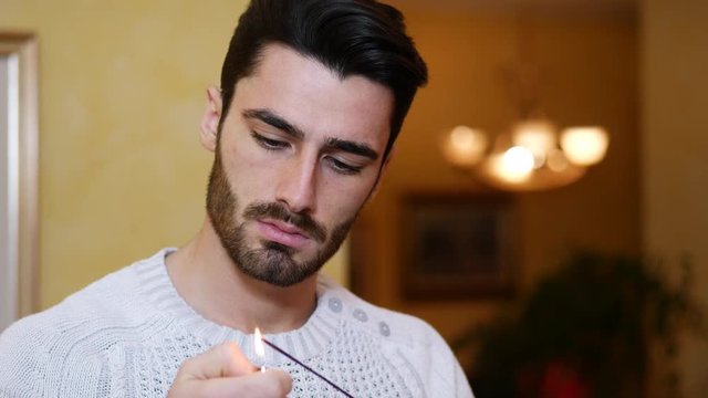 Cheerful handsome man standing with joss stick or incense at home.
