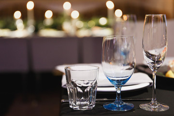 Close up three glasses, forks, knives, napkins, candles and decorative flower on dark black tablecloth on table served for dinner in cozy restaurant. Empty served restaurant table with wine glass.