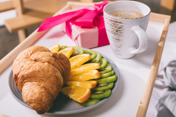 tray with croissant and fruits and present box on bed