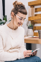 smiling girl sitting on chair and looking at smartphone in office