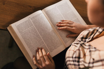 Obraz premium in the foregraund there are a large book and a girl' s plaid shirt and hands with a beautiful neat manicure.