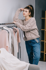 girl leaning on stand with clothes and looking away