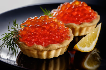 Tartlets with red caviar on black background
