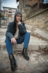 girl in boots and jeans sitting on steps with knitted hat on head 