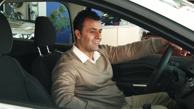 A man is sitting at the steering wheel of a car. He examines the salon. The man has satisfied and happy face