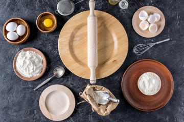 flat lay with rolling pin, wooden plates and bakery ingredients on dark surface