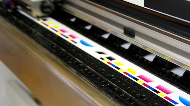 Plotter head printing CMYK test on white paper. Digital large inkjet machine working.