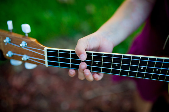 closeup of hand of young child playing acoustic guitar in park outdoor at sunset