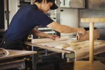 Man working in a bakery, cutting dough for rolls with large cutter.