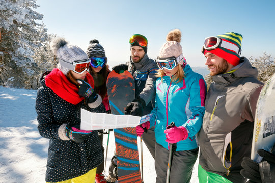 friends reading a paper map in winter holidays in snowy mountain
