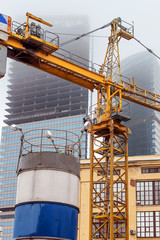 Fototapeta premium a crane at a construction site in foggy weather, on the background of the unfinished skyscrapers