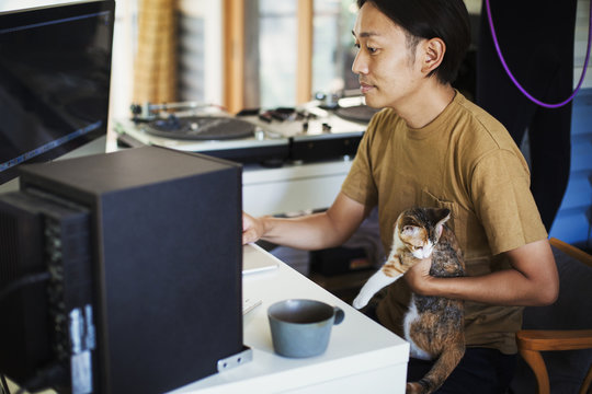 Man sitting at a desk in front of computer, calico cat with white, brown and black fur on his lap.